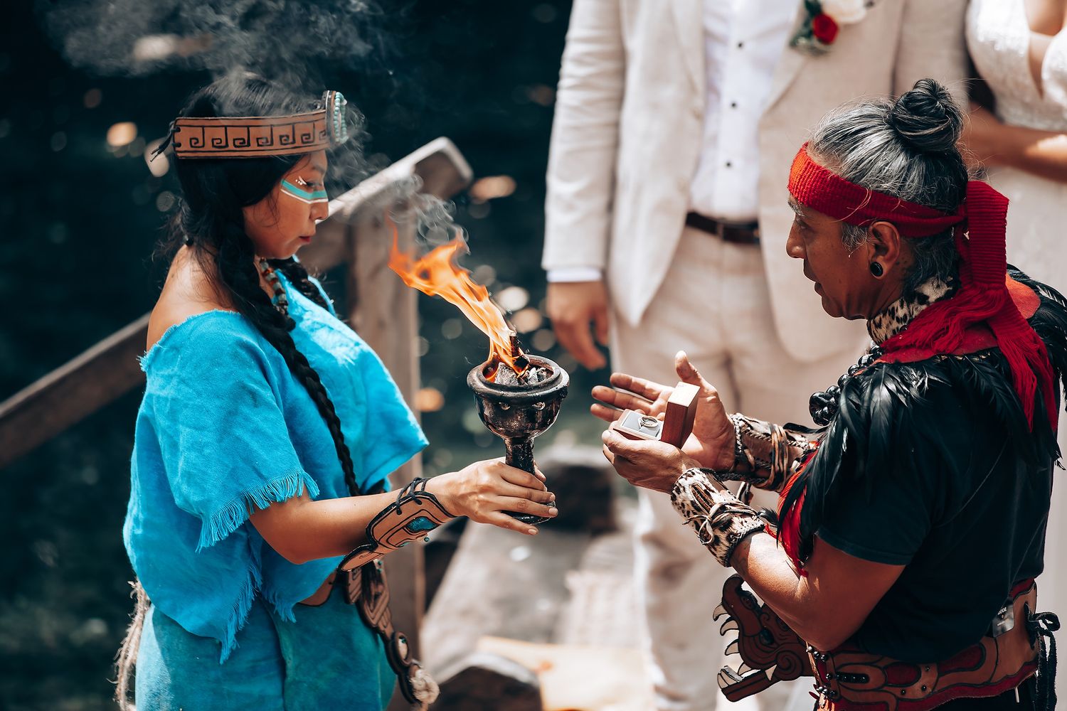 Traditional ceremony participants performing rituals with fire and offerings in an outdoor setting.