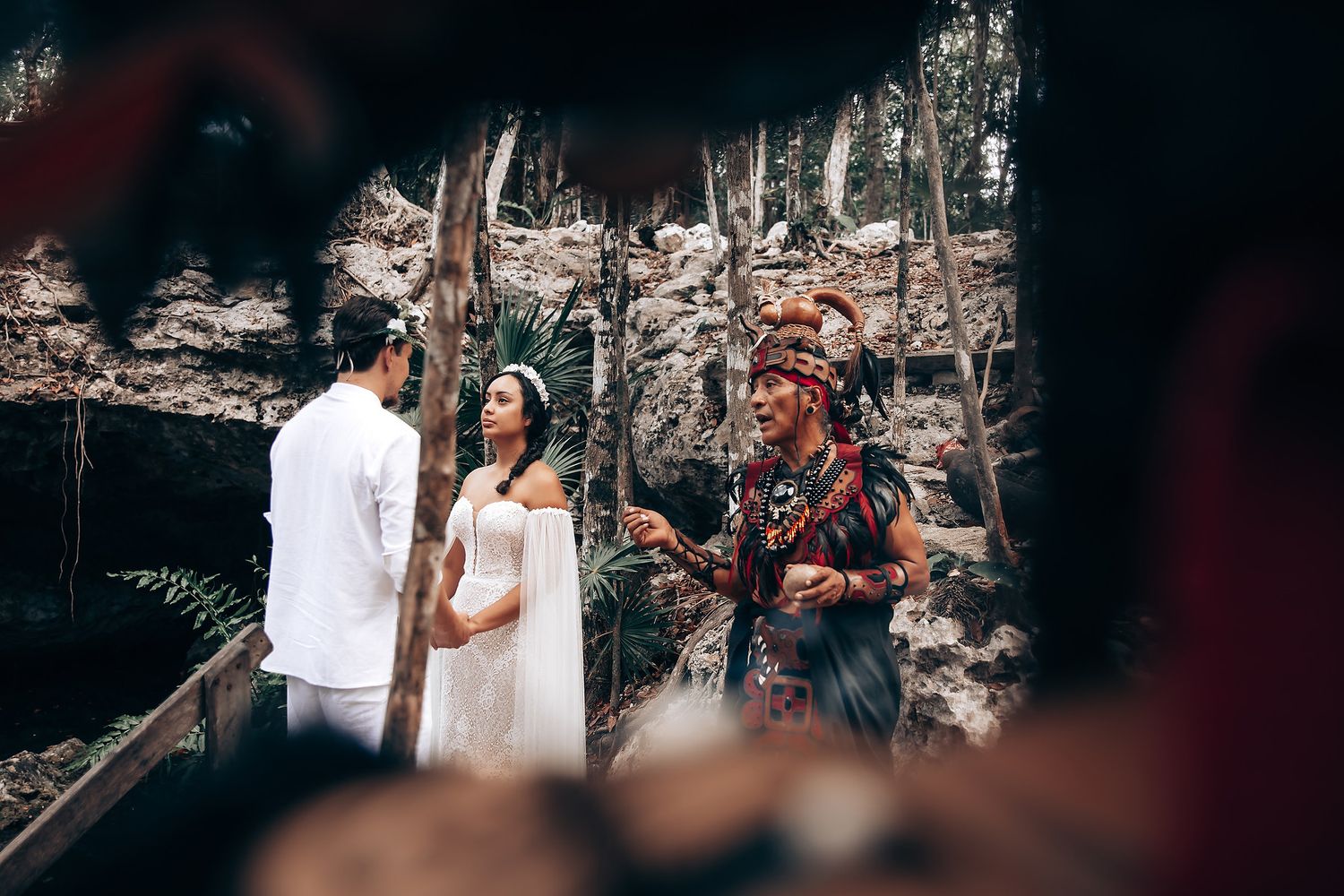 Wedding ceremony taking place on a wooden platform with natural stone walls and tropical vegetation.