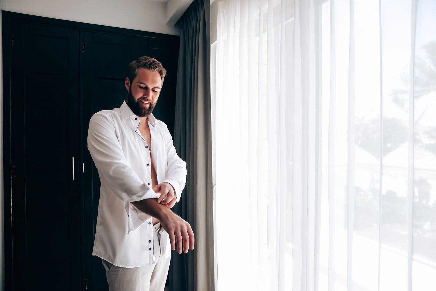 A person in a white shirt stands by a window in a dramatic black and white portrait series.