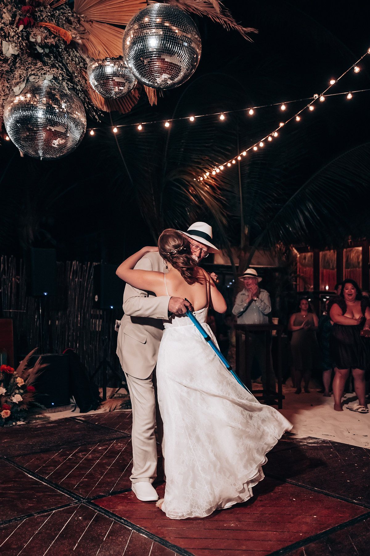 Couple dancing under disco balls and string lights at a beach wedding reception.