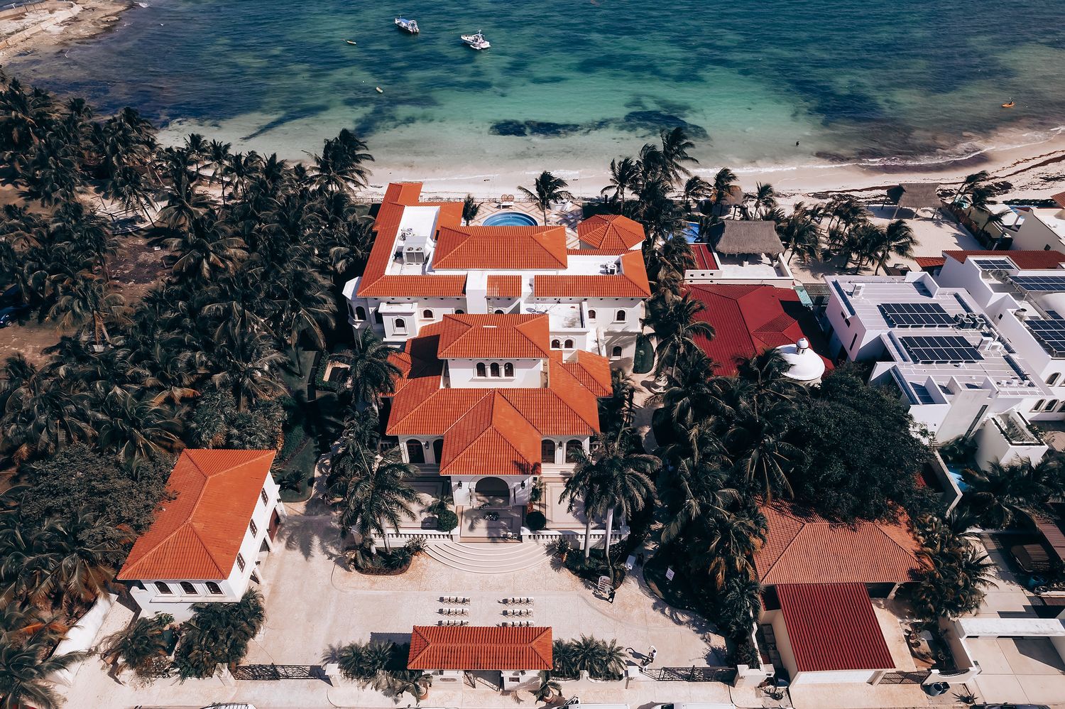 Aerial view of coastal homes with red tile roofs surrounded by palm trees and beaches.