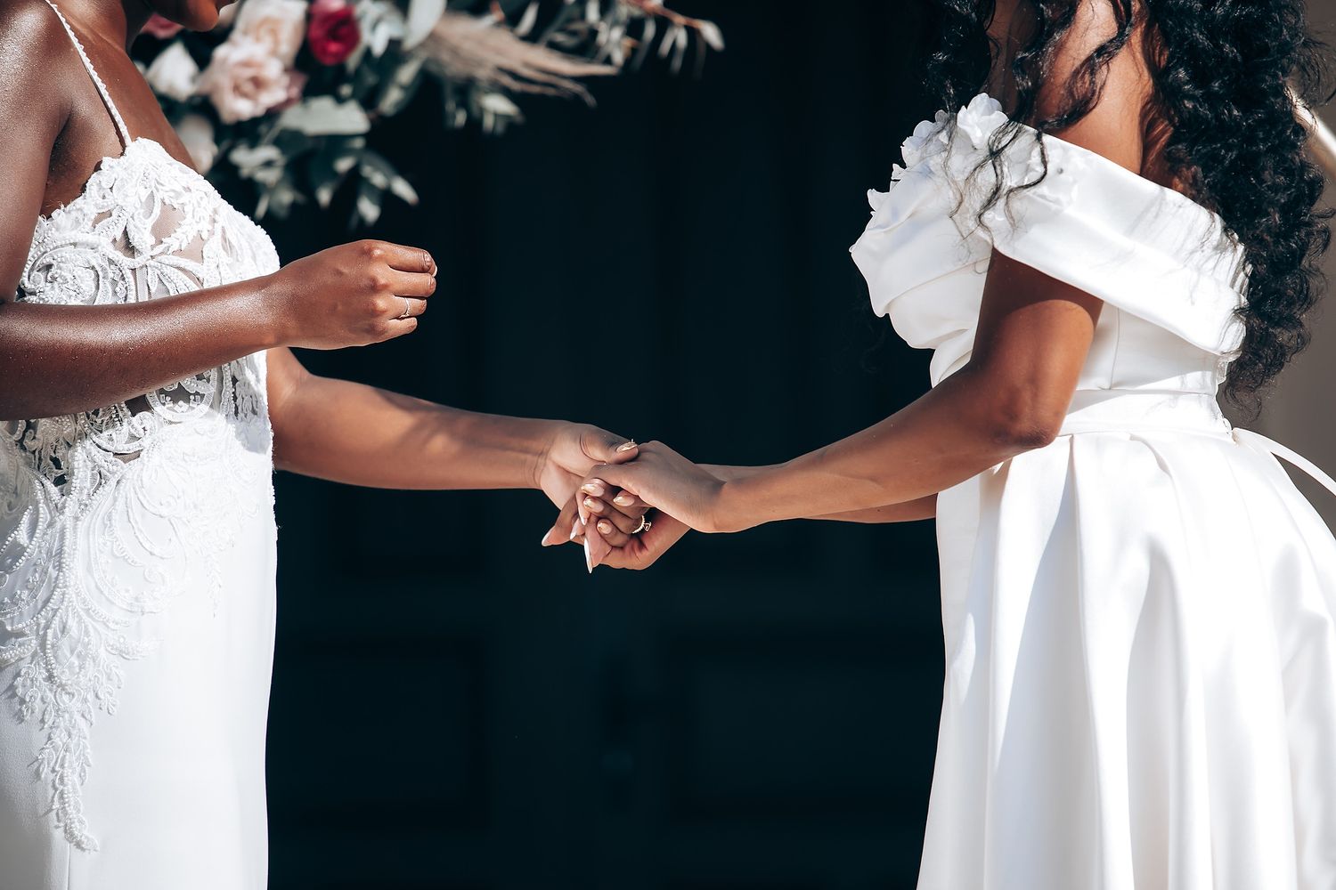 Close-up of two people holding hands while wearing elegant white dresses.