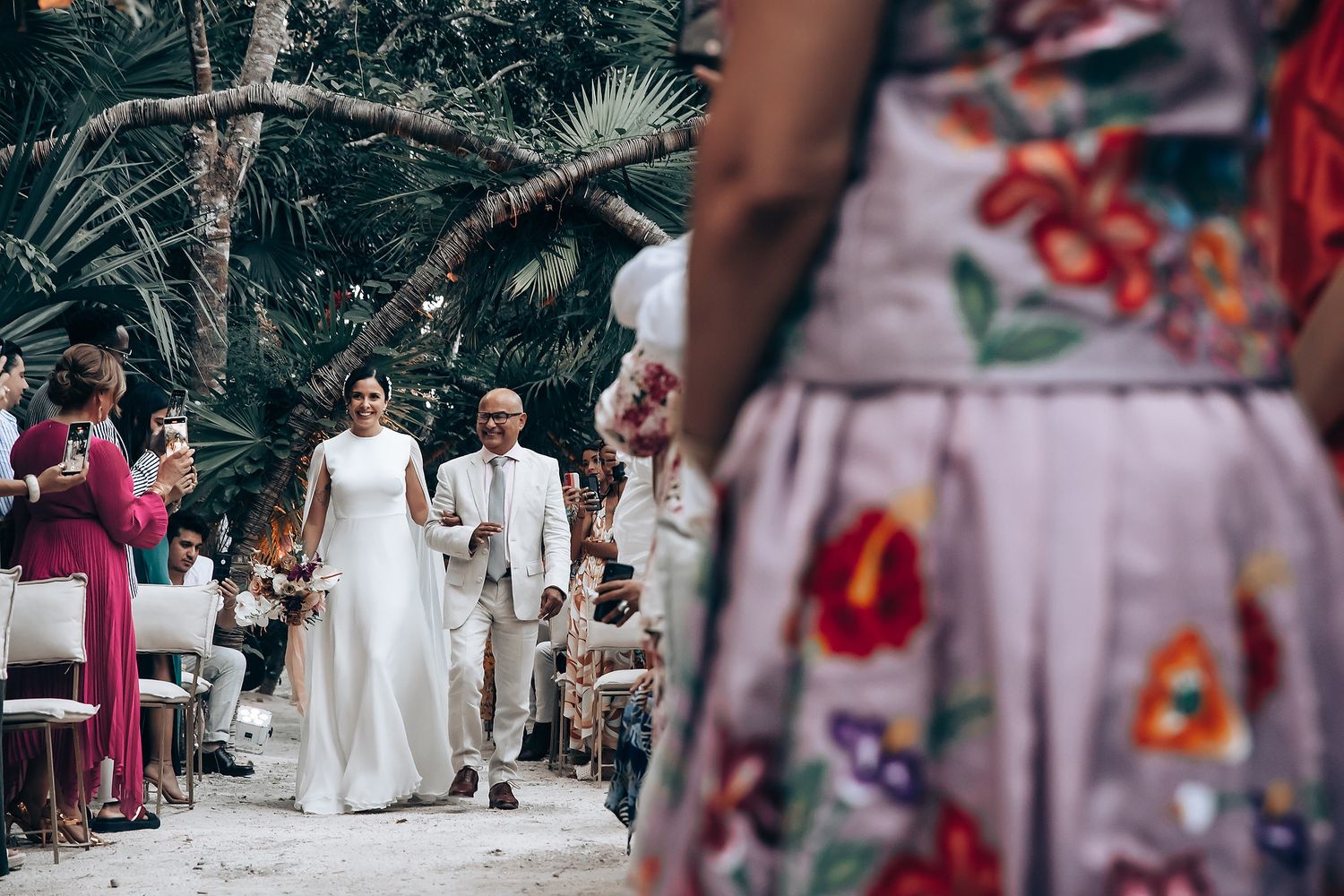 Tropical garden wedding ceremony with palm trees and guests in colorful attire.