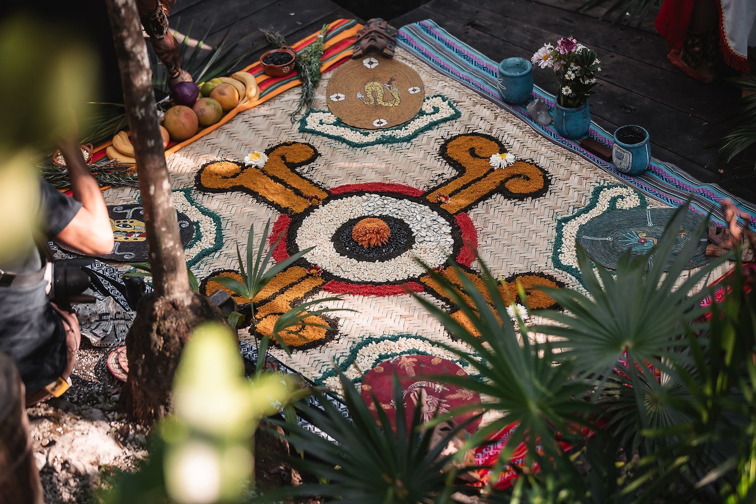 Colorful mosaic floral carpet with intricate patterns displayed outdoors among tropical plants.