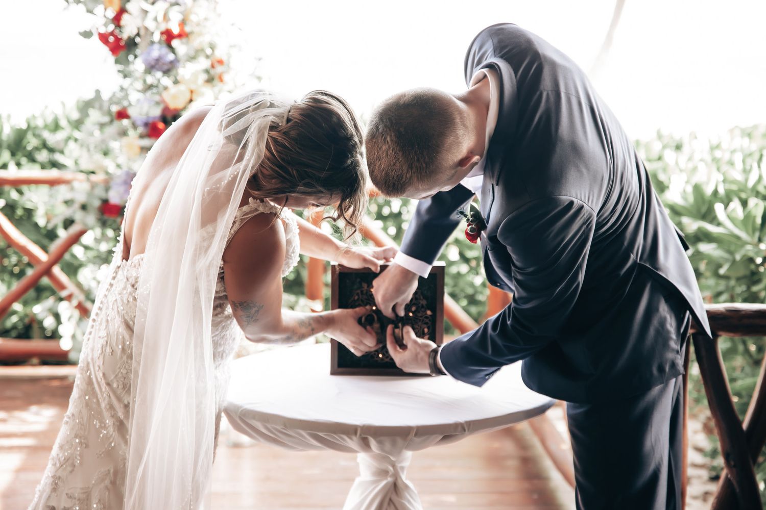 Bride and groom signing wedding documents together at a white table during outdoor ceremony.