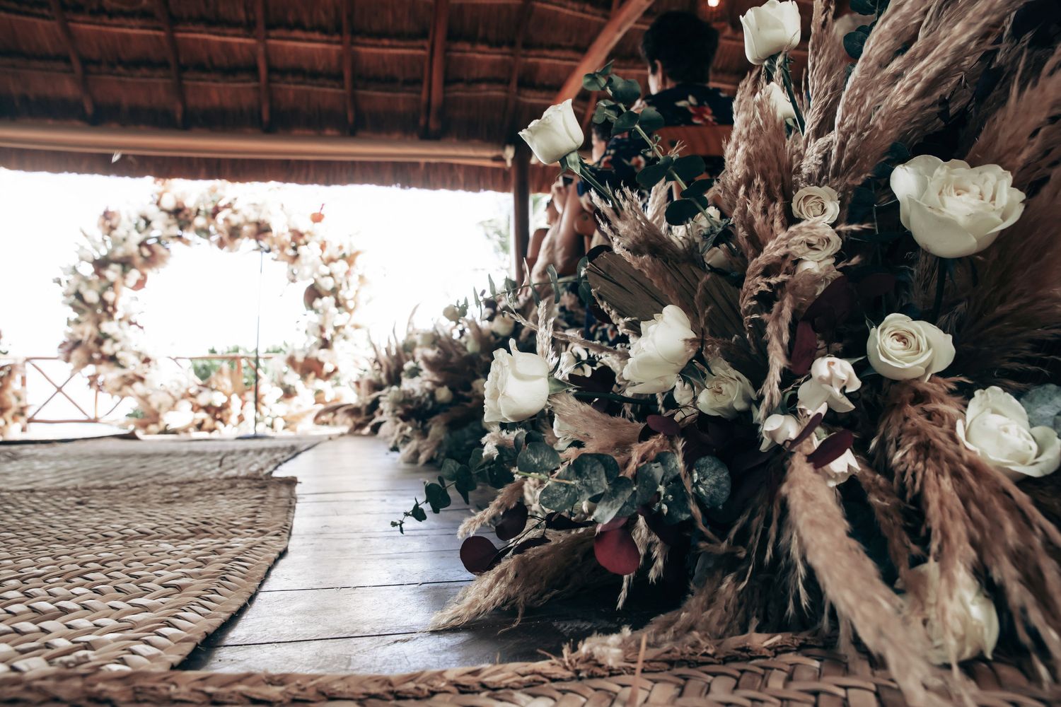 Rustic boho wedding ceremony arch adorned with dried pampas grass and white roses at an outdoor venue at Dreams Tulum