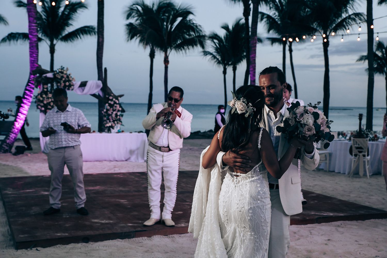 An evening beach reception with palm trees and purple lighting creating a romantic atmosphere.