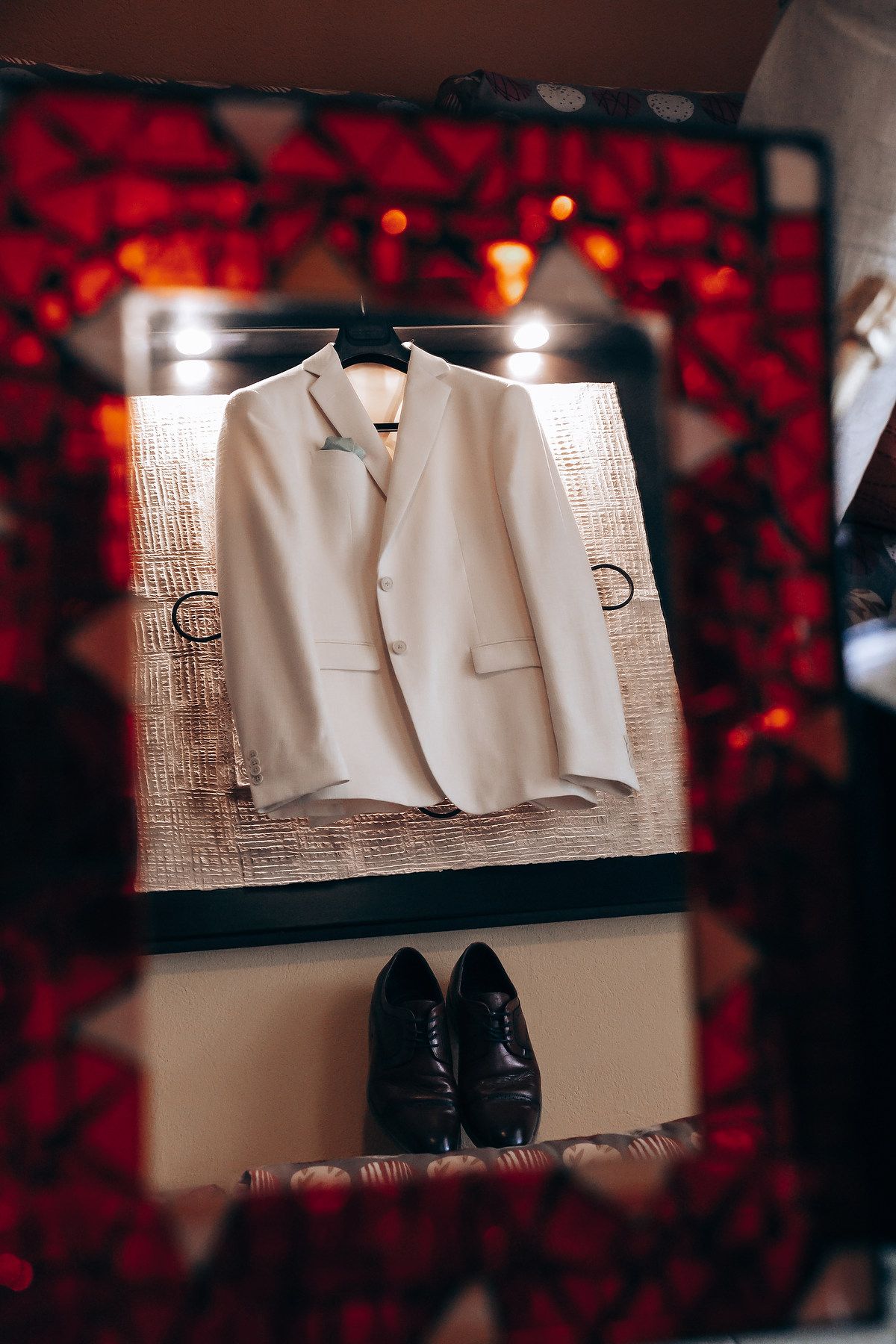 A white suit jacket and black dress shoes displayed against a red bokeh background.