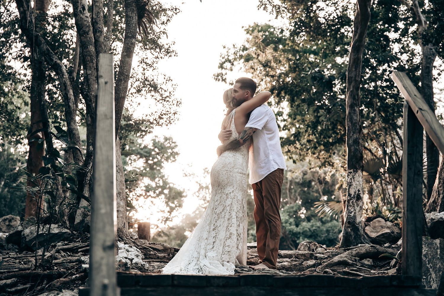 A romantic outdoor photoshoot captures intimate moments among tall trees in natural light.
