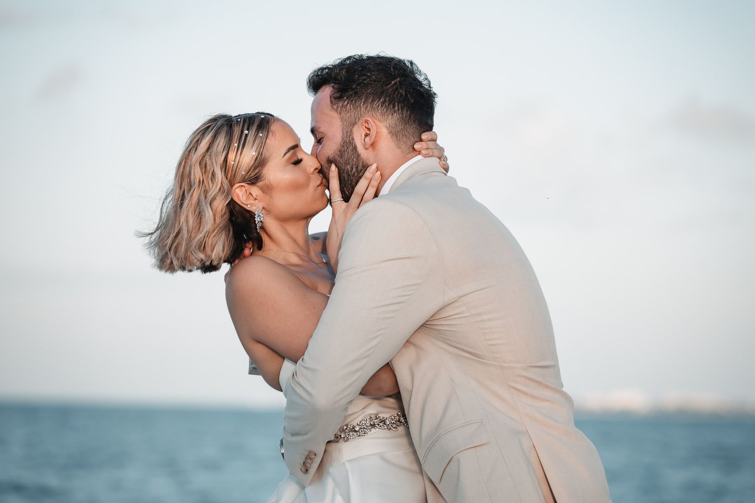 Bride and groom sharing romantic kiss by the ocean at tropical beach wedding celebration.