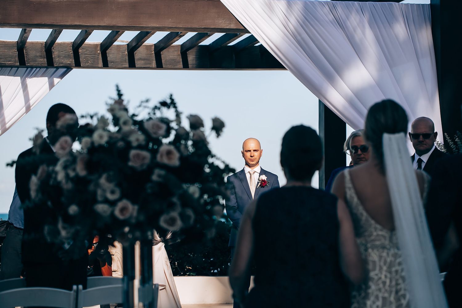 A wedding ceremony taking place outdoors with the couple standing under a floral arch.