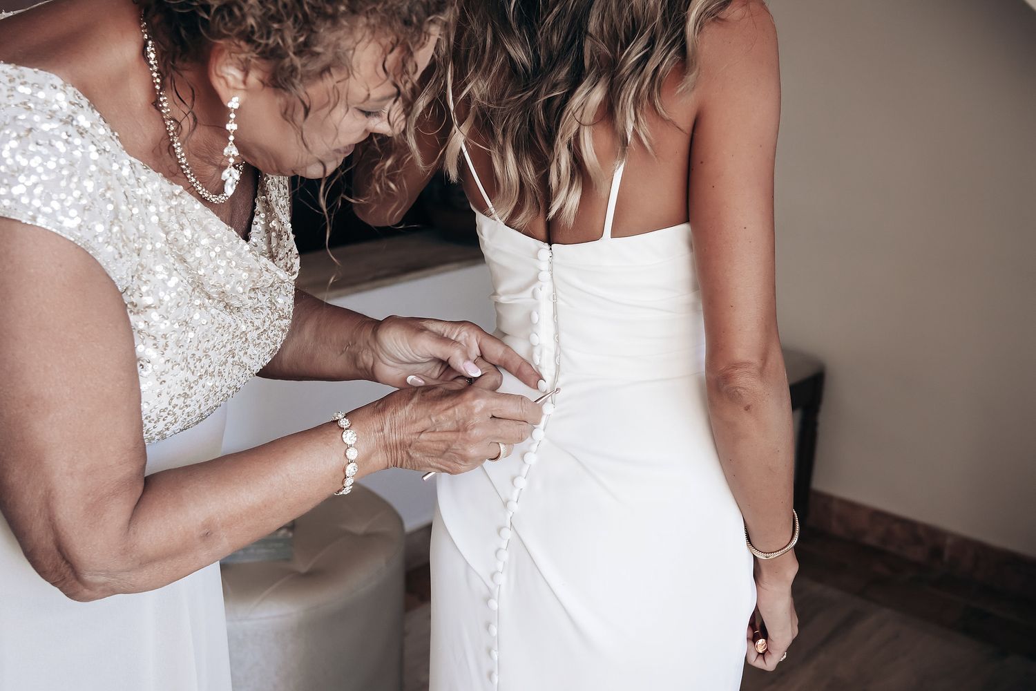 A woman in a white dress is being helped into her dress by another person.
