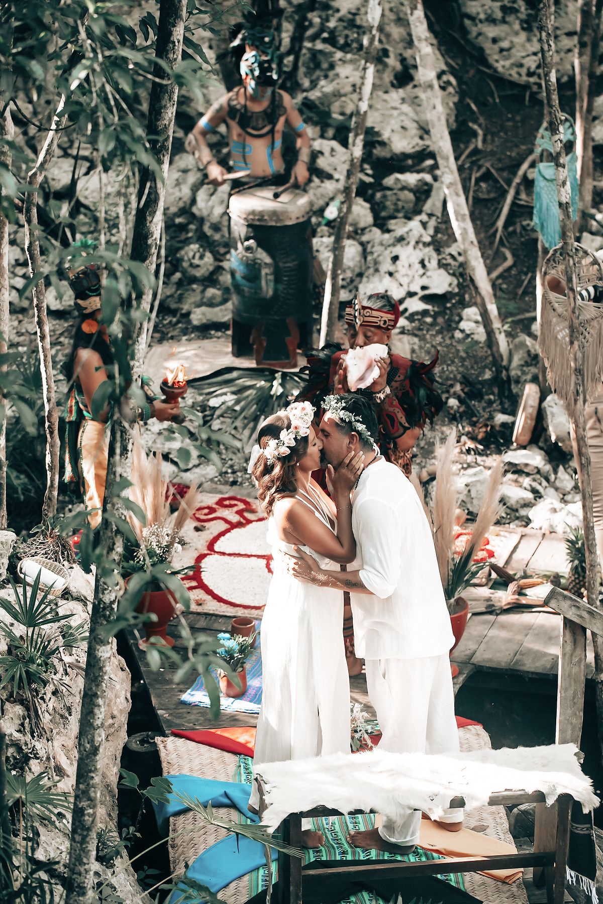 A person in traditional dress performs a ceremony for a couple in a tropical forest setting.