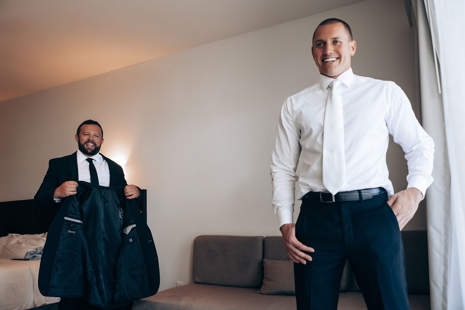 A groom adjusts his formal black suit and tie while preparing for the wedding ceremony.