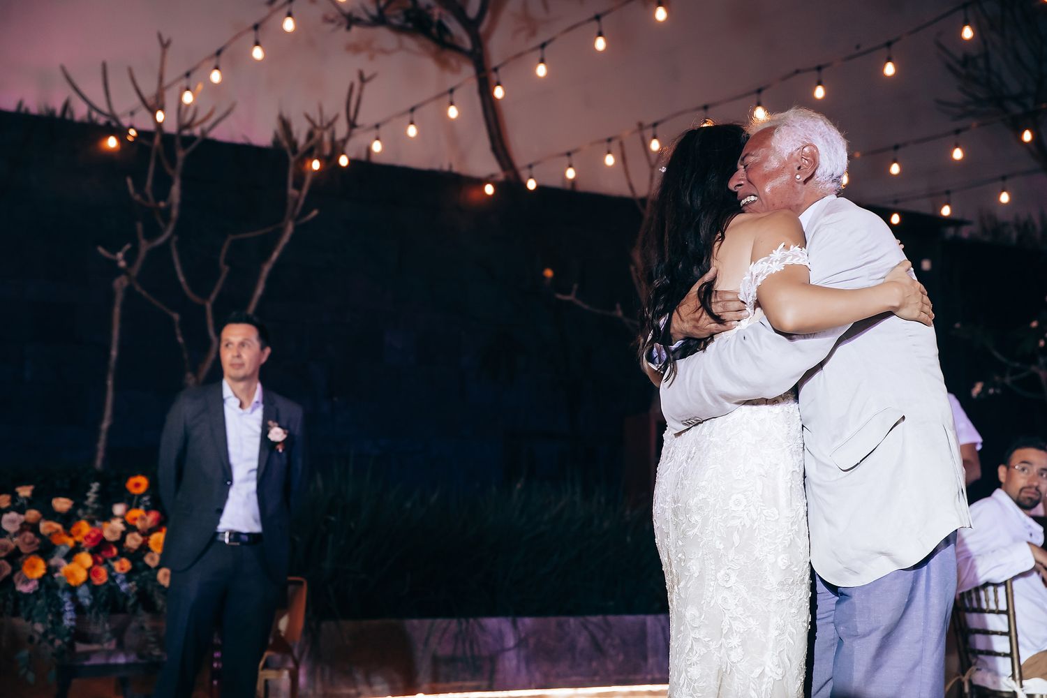 Wedding guests dance together under twinkling string lights at an outdoor evening reception.