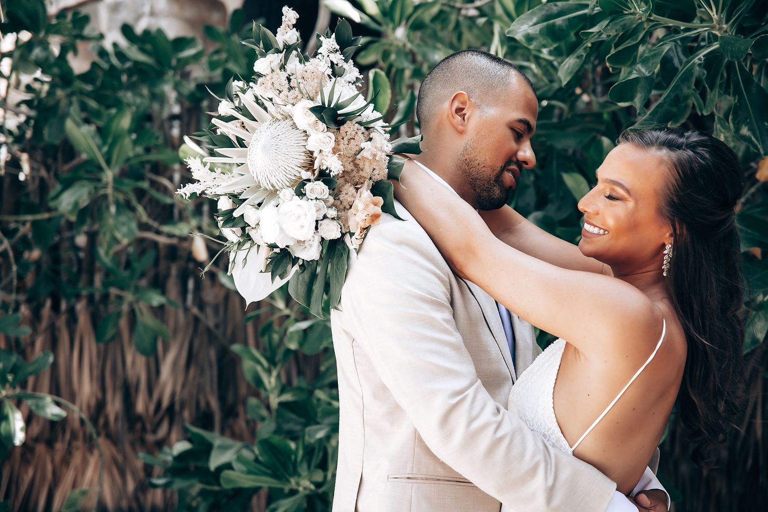 Romantic wedding couple embraces in a lush tropical garden setting with natural greenery and flowers.