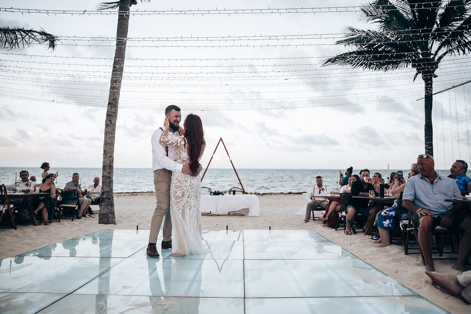 Beachfront wedding setup with white chairs and palm trees against ocean backdrop.