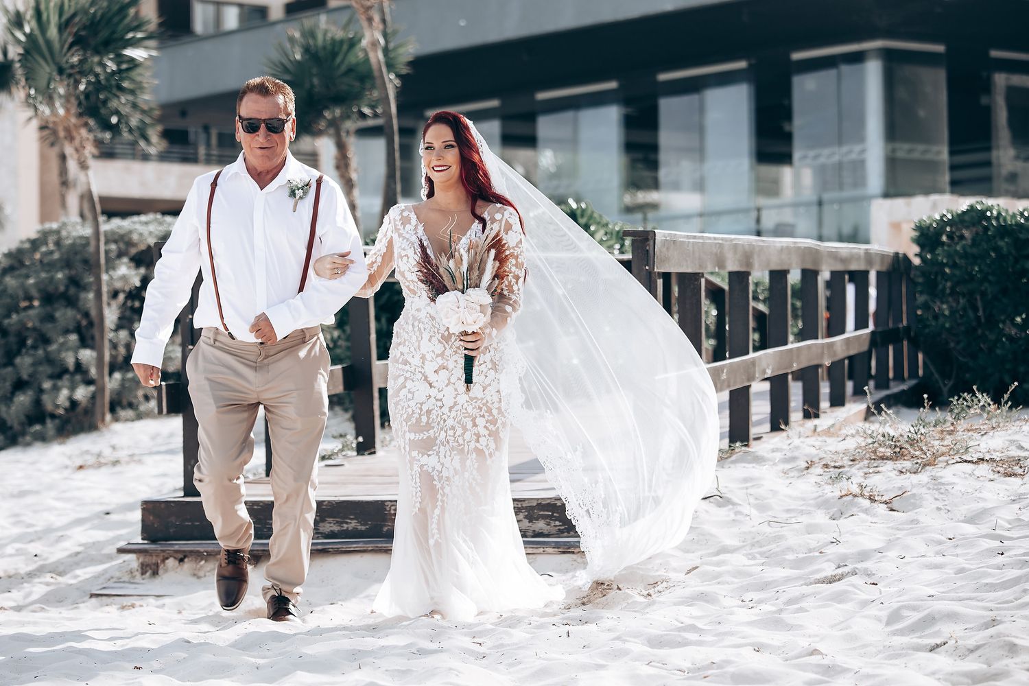 Couple and wedding party strolling through soft sand during beach wedding celebrations.