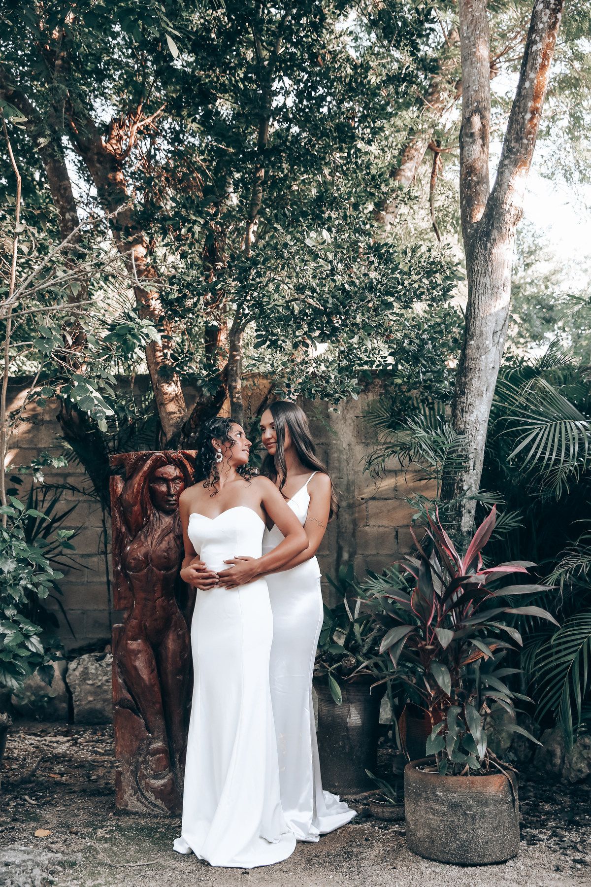 A romantic garden photoshoot featuring two people in white dresses among tropical foliage.
