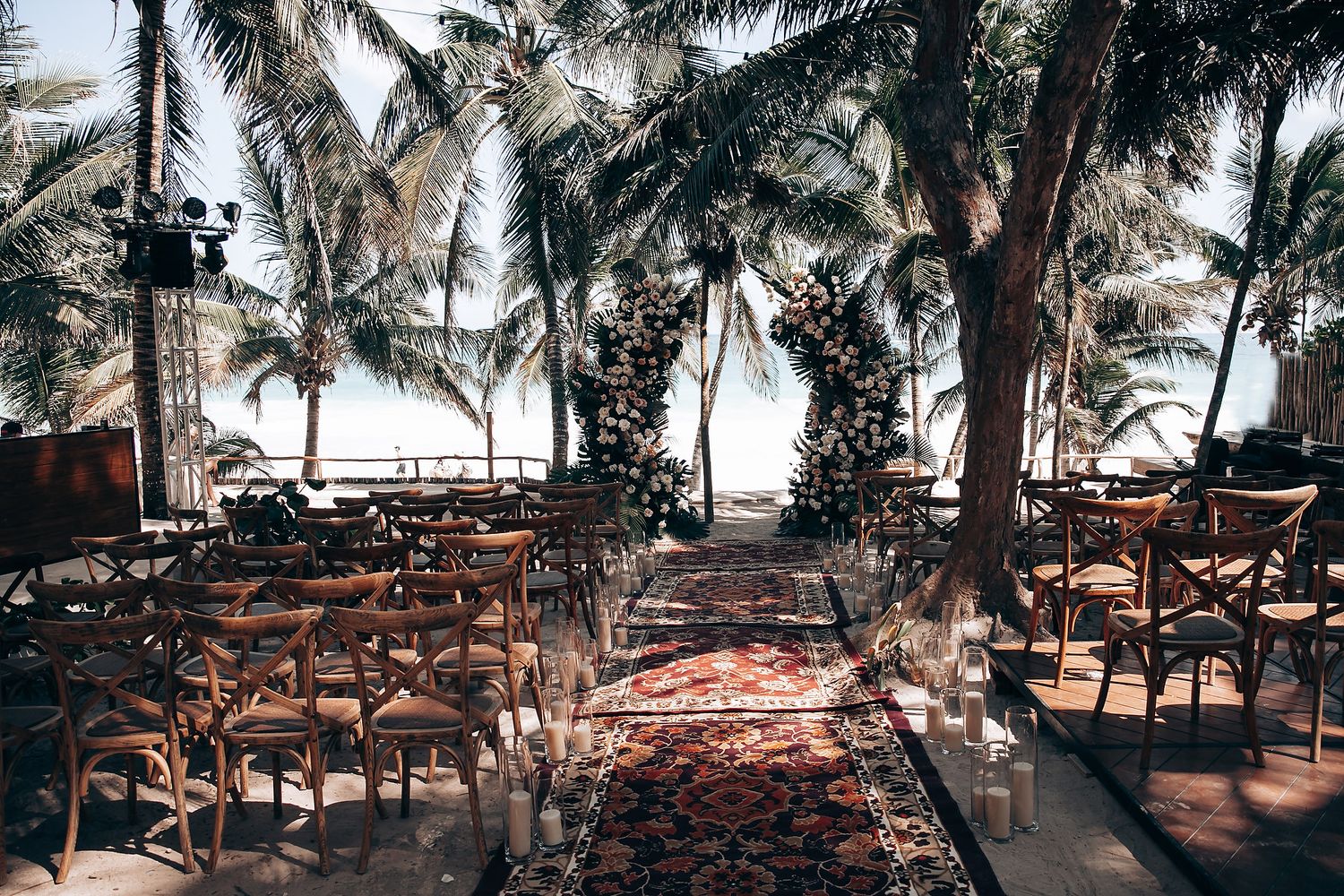 A row of wooden beach lounge chairs under palm trees at a tropical resort during sunset.