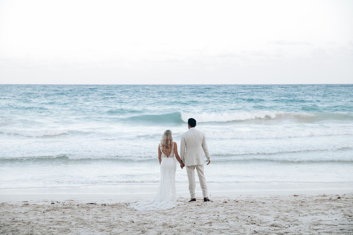 Couple walking along serene beach with gentle waves in background.