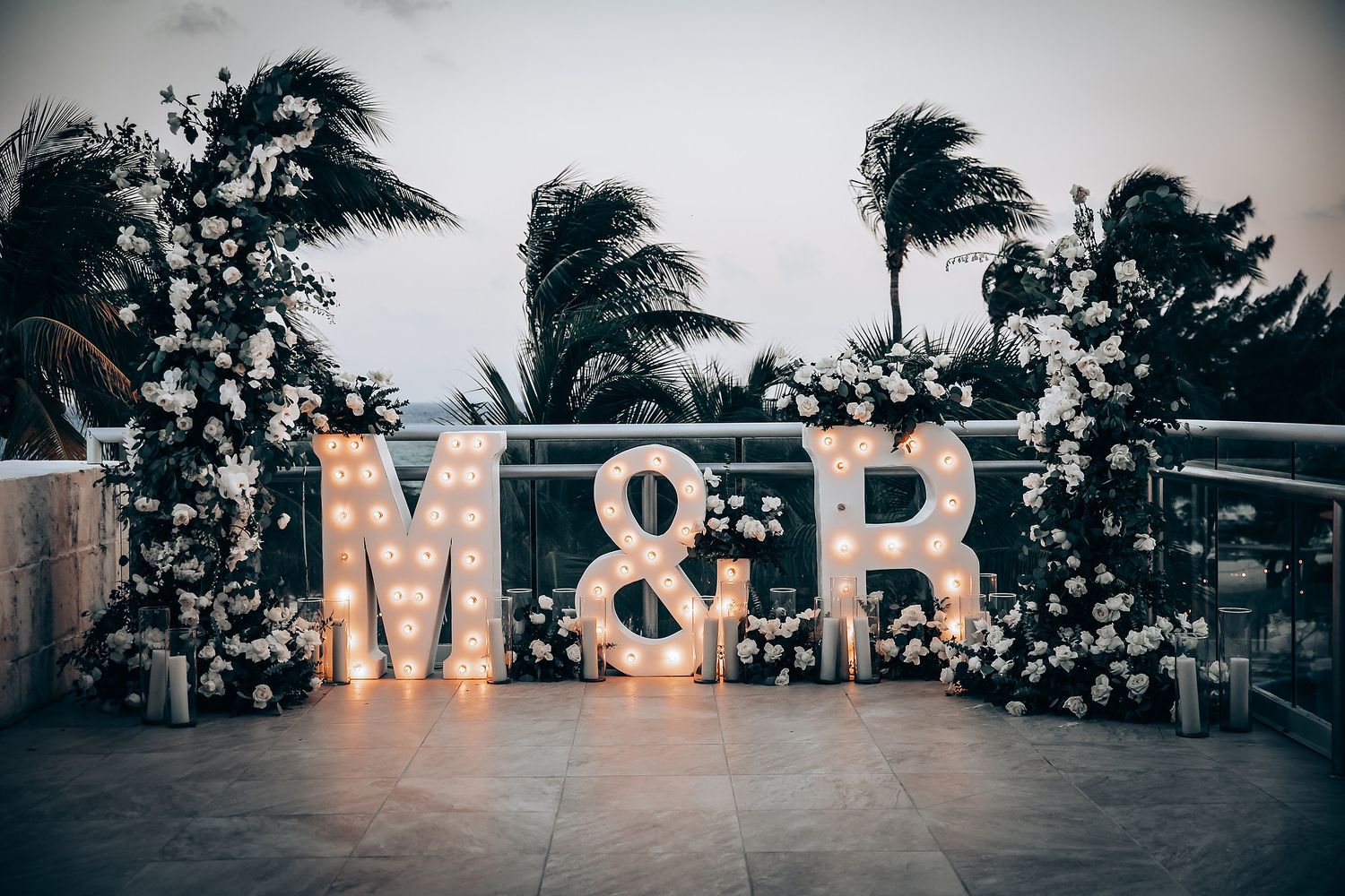 Illuminated marquee letters spelling M&R at dusk with palm trees in background.
