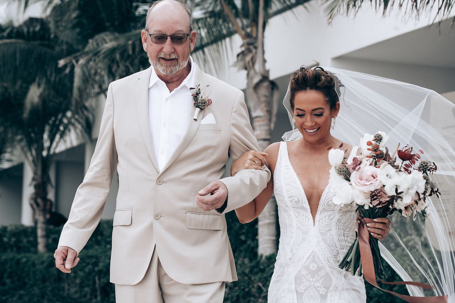 Wedding ceremony attendees gathered under palm trees at a tropical beach location.