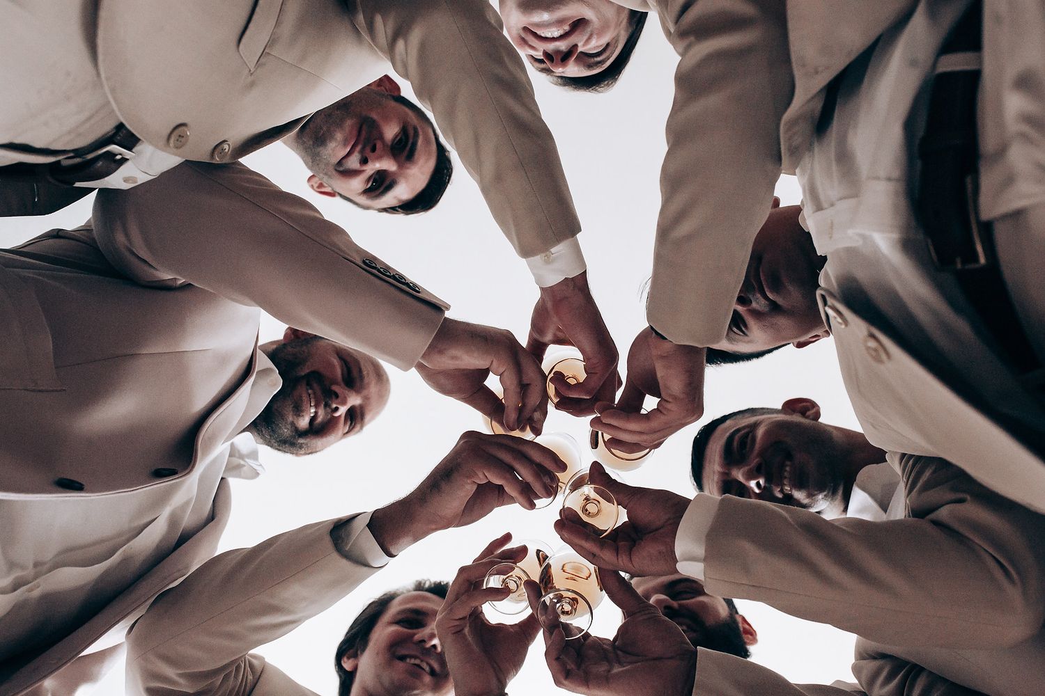 Group of hands coming together in a circle for a celebratory toast with champagne glasses from below.