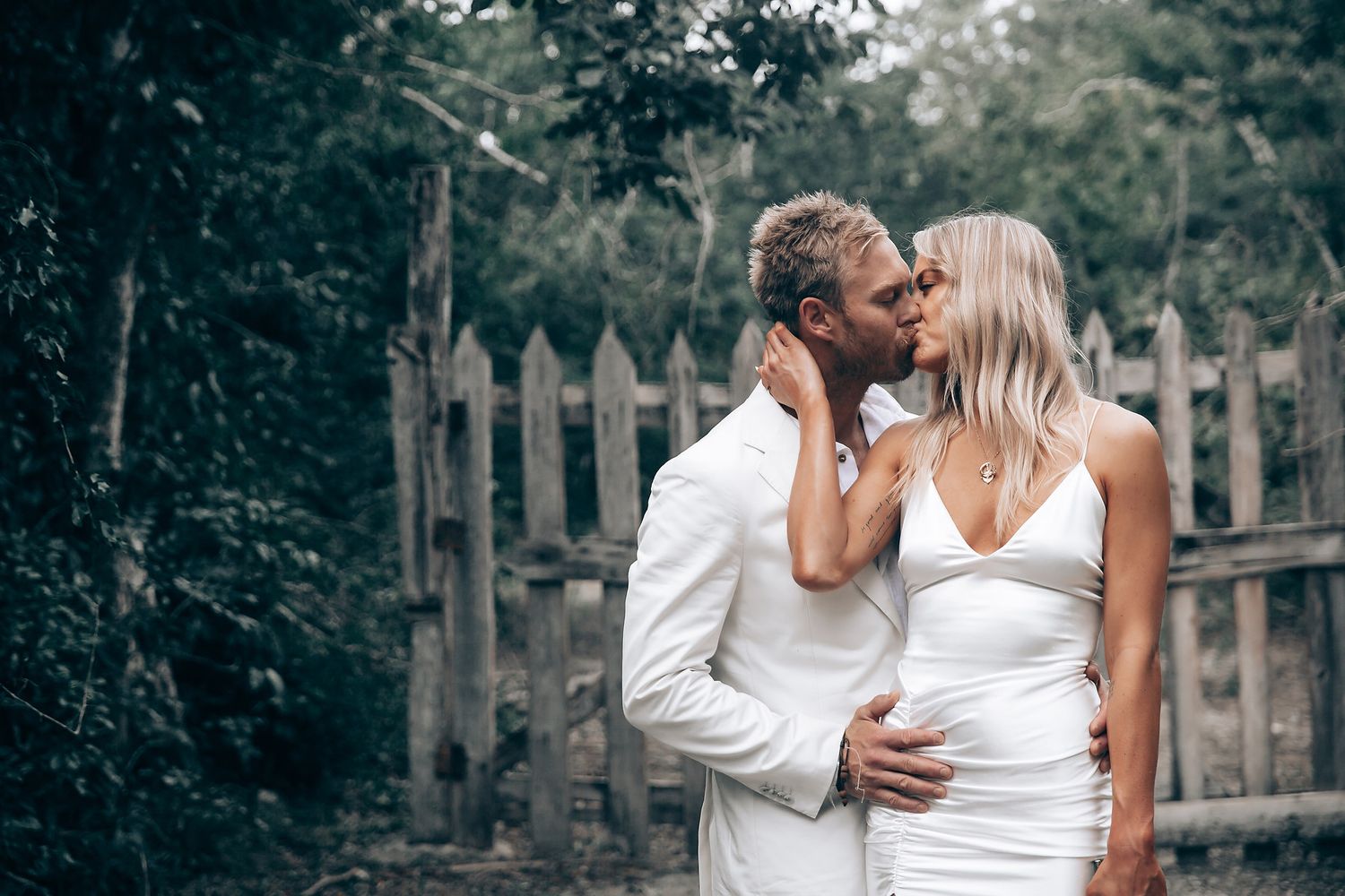An intimate wedding portrait against a rustic wooden fence in a garden setting.