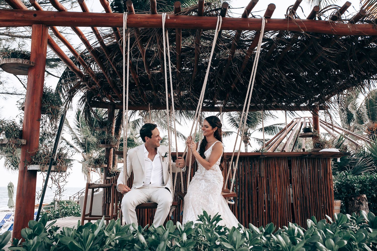 Couple shares intimate moment on wooden swing beneath tropical garden pergola.