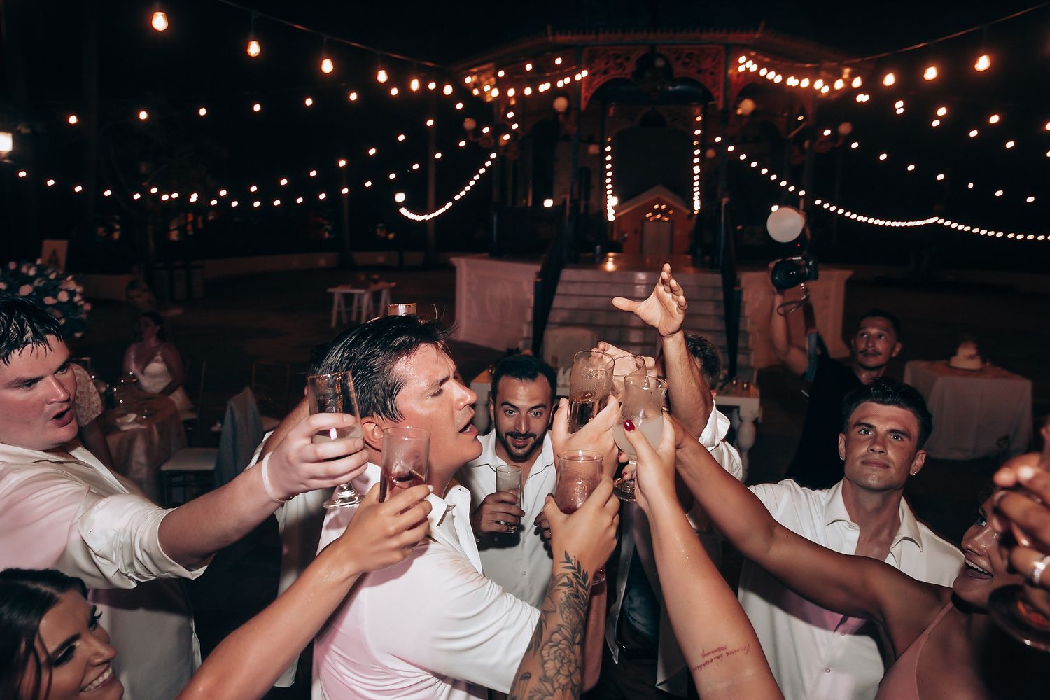 Wedding reception dance floor filled with guests celebrating under glowing string lights.