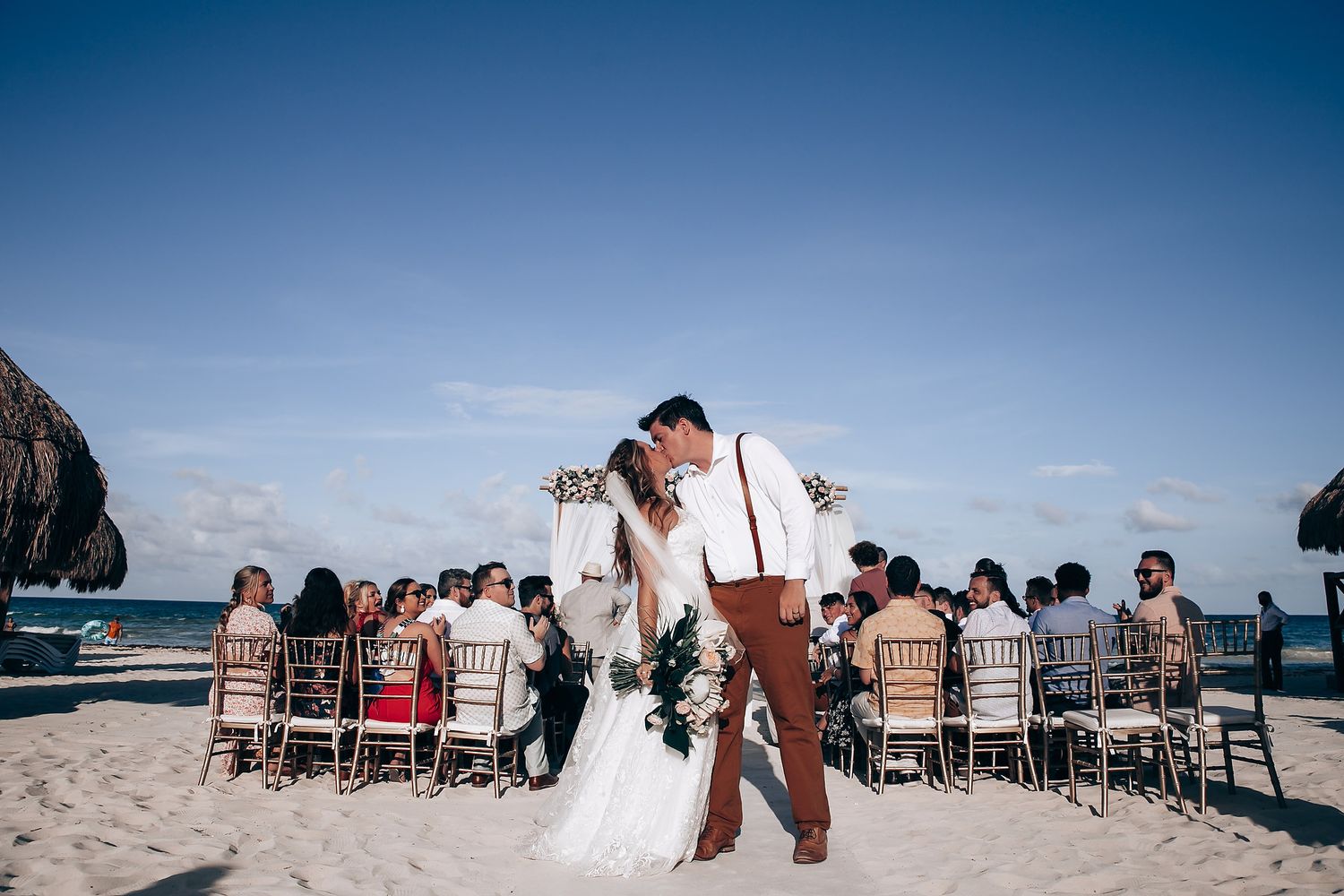 Wedding guests seated on beach chairs watch oceanfront ceremony.