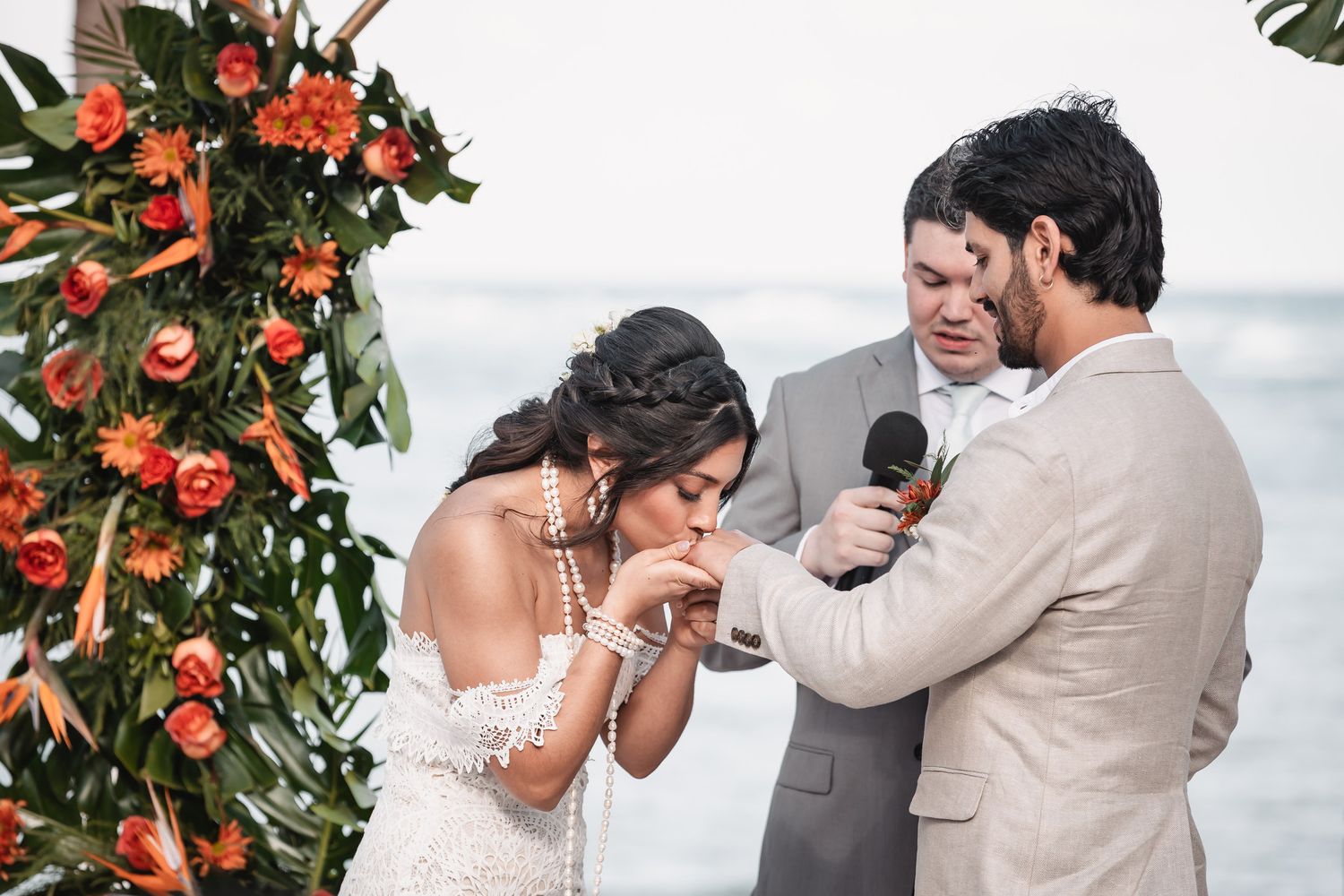 Bride and groom exchange vows at tropical beach wedding with vibrant orange floral arch.
