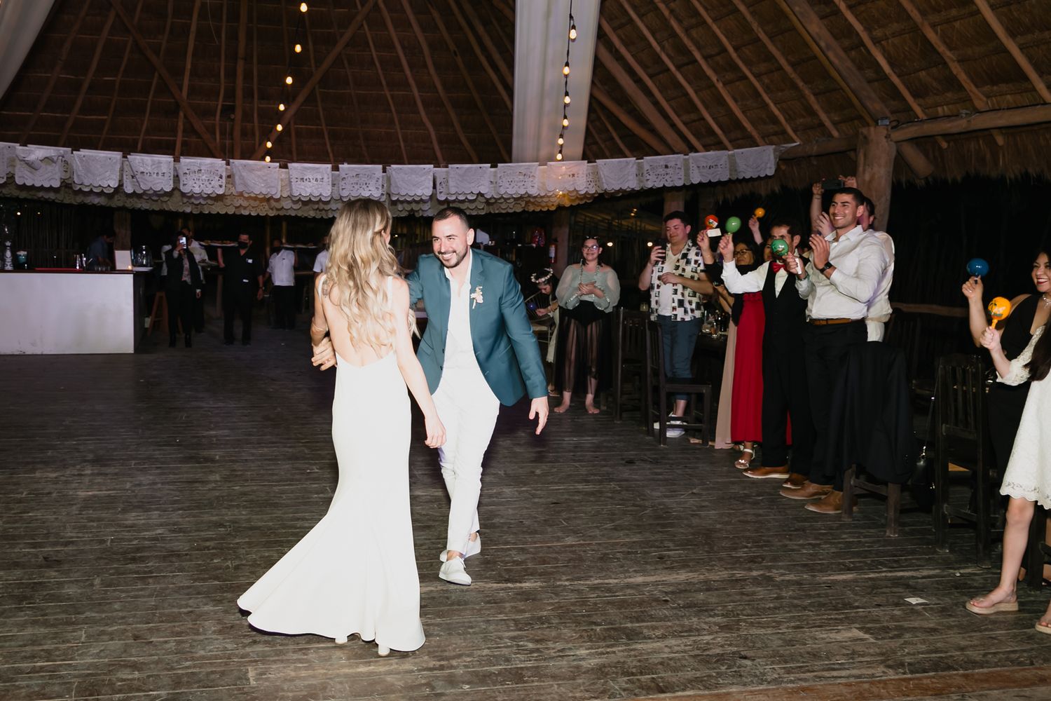 Bride and groom making grand entrance onto wooden dance floor at tropical wedding reception.