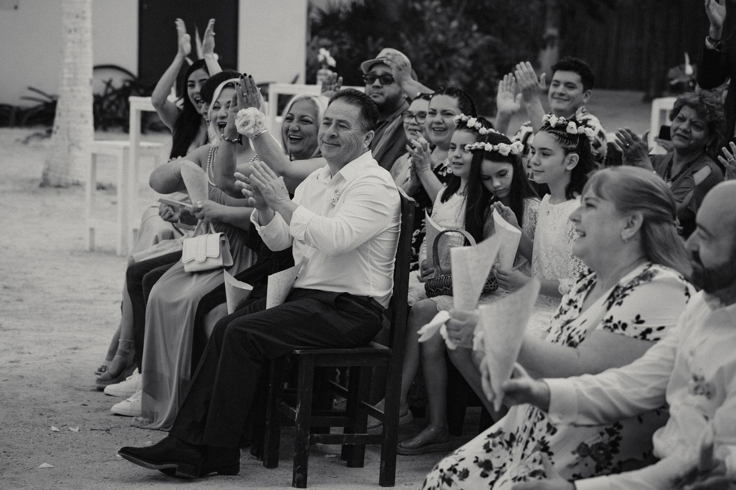 Black and white photo of joyful wedding guests clapping and celebrating during an outdoor beach ceremony.