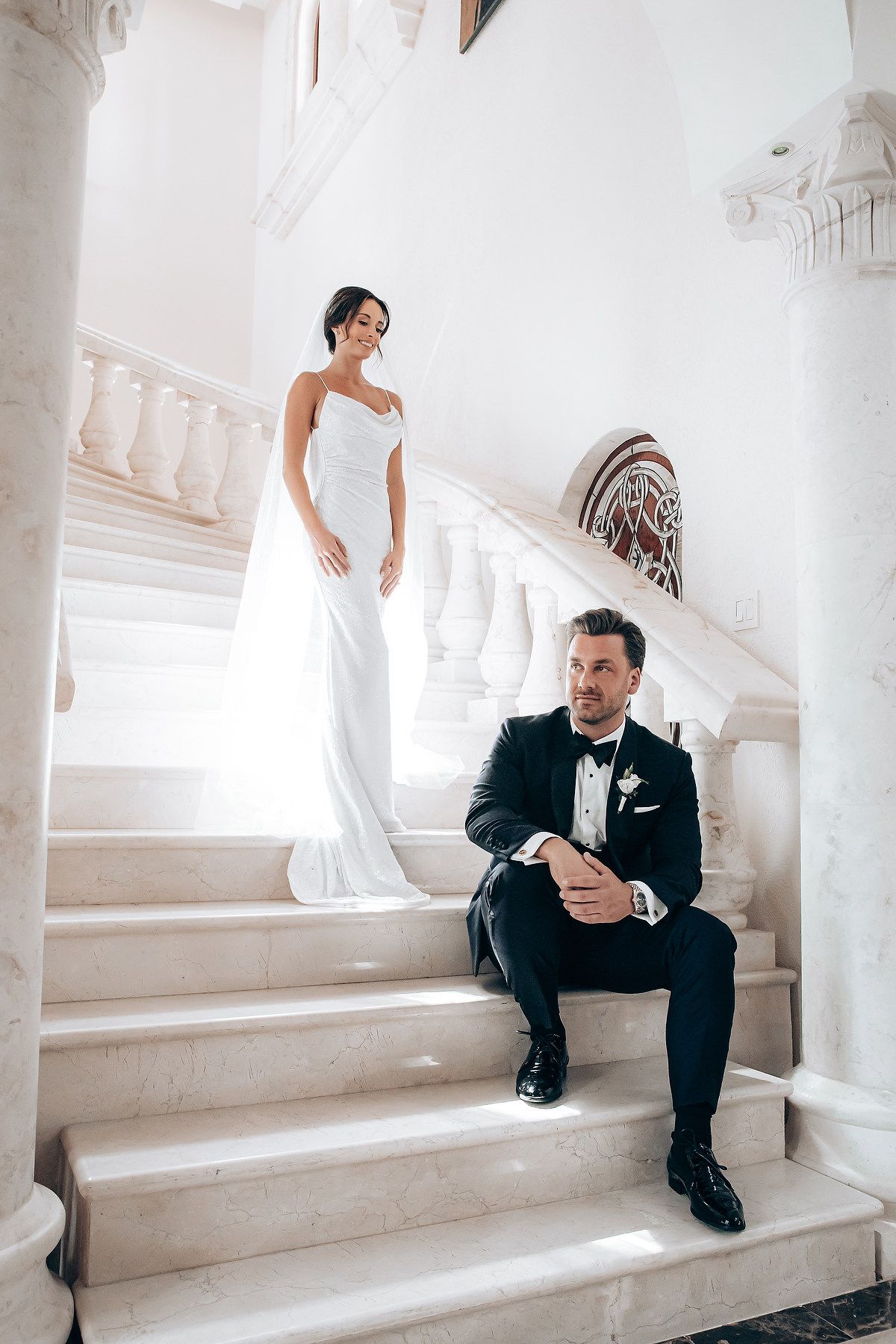 Elegant wedding photo session on white marble staircase with classical columns.