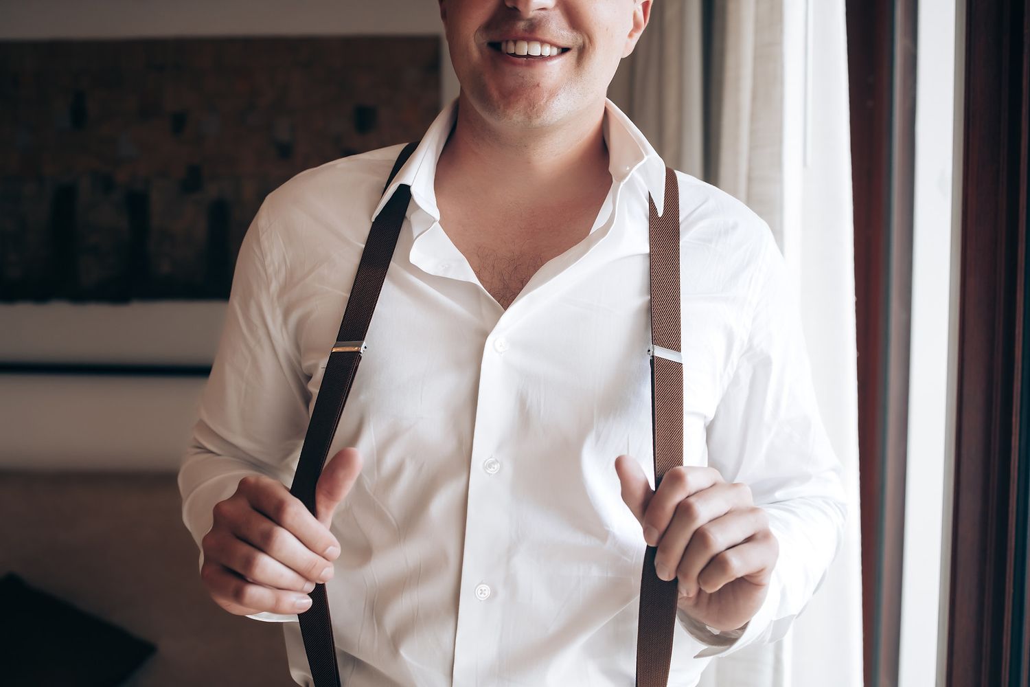 A person in a white shirt smiles while holding a drink near a window in what appears to be a cafe setting.