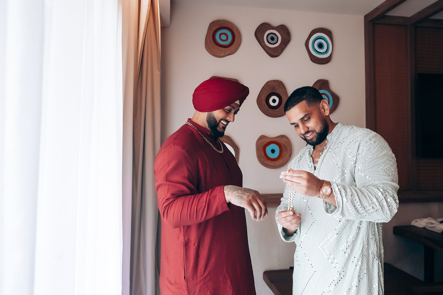 Two men in traditional Indian attire examining something together indoors.