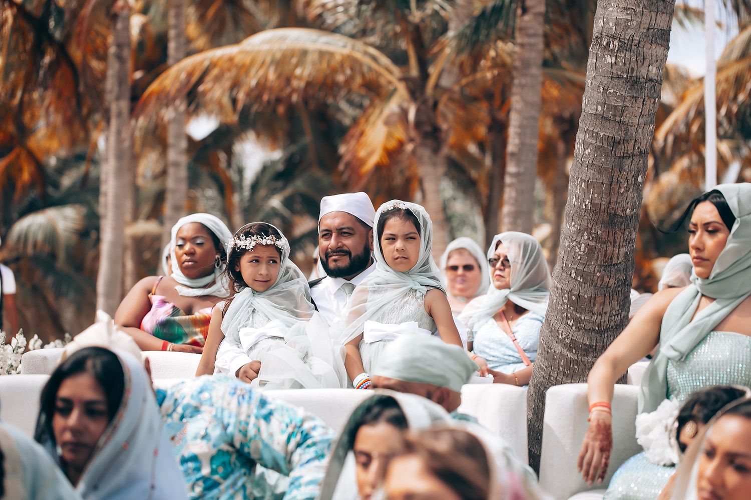 Guests seated outdoors for a beach wedding ceremony with palm trees and ocean views.