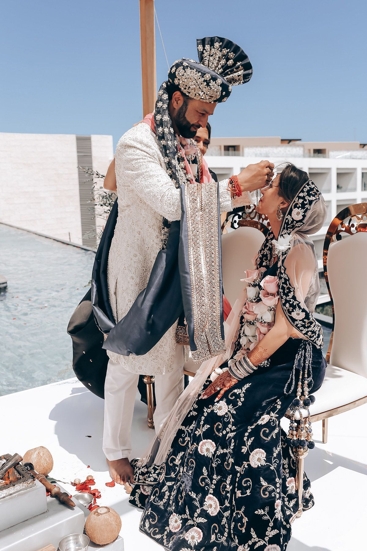 A romantic moment captured between newlyweds in traditional Indian wedding attire on a white terrace.