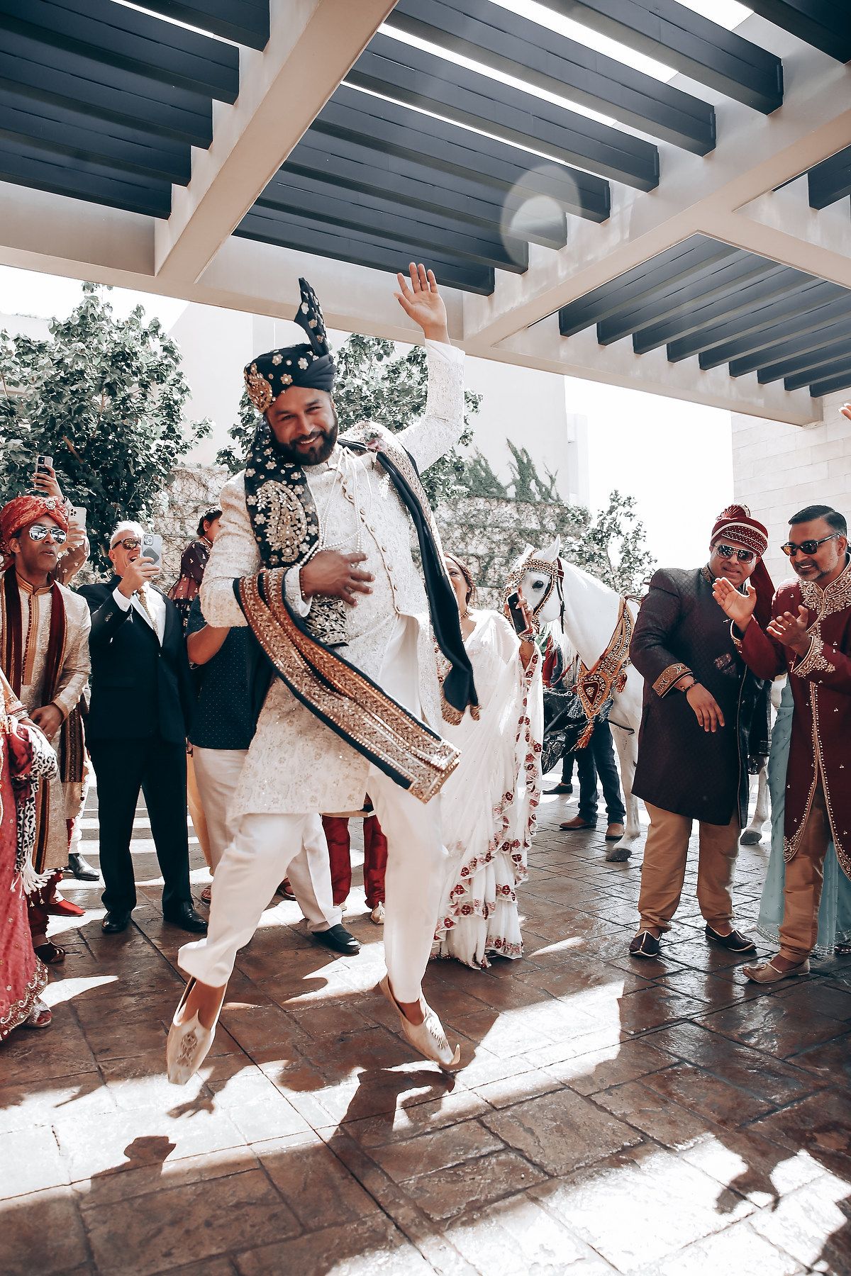 Wedding guests dance and celebrate in a joyful line under a covered outdoor patio area.