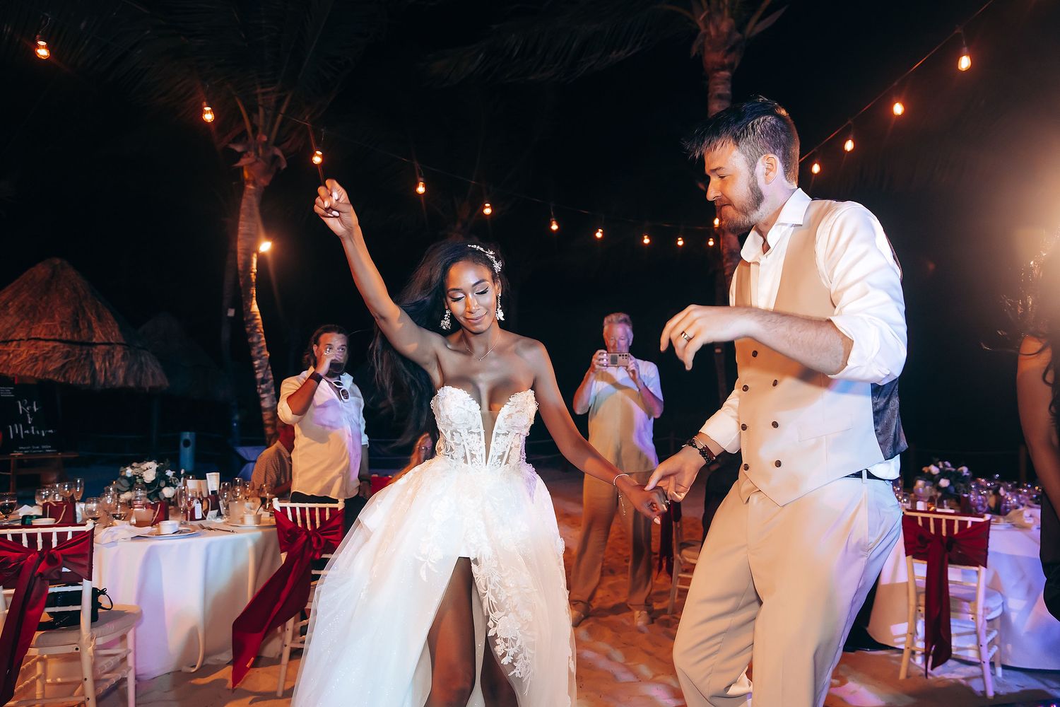 Wedding party dancing and celebrating during nighttime reception under string lights.