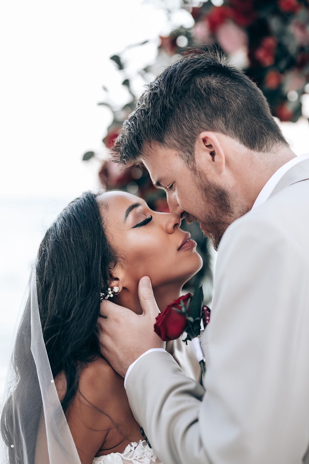 Romantic wedding moment under an arch decorated with red and pink roses.