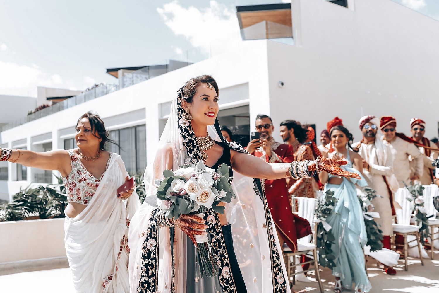 Wedding guests celebrate and dance together during a joyful reception party on a sunny outdoor terrace.