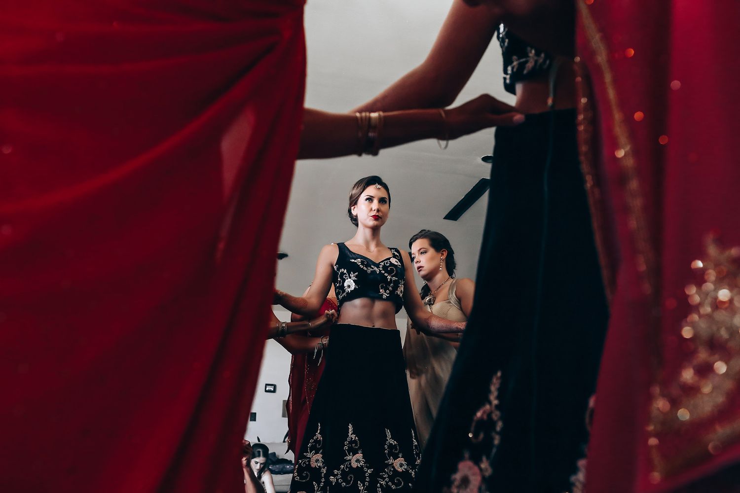 Professional ballet dancers perform graceful movements in black costumes on a dimly lit stage with red lighting.