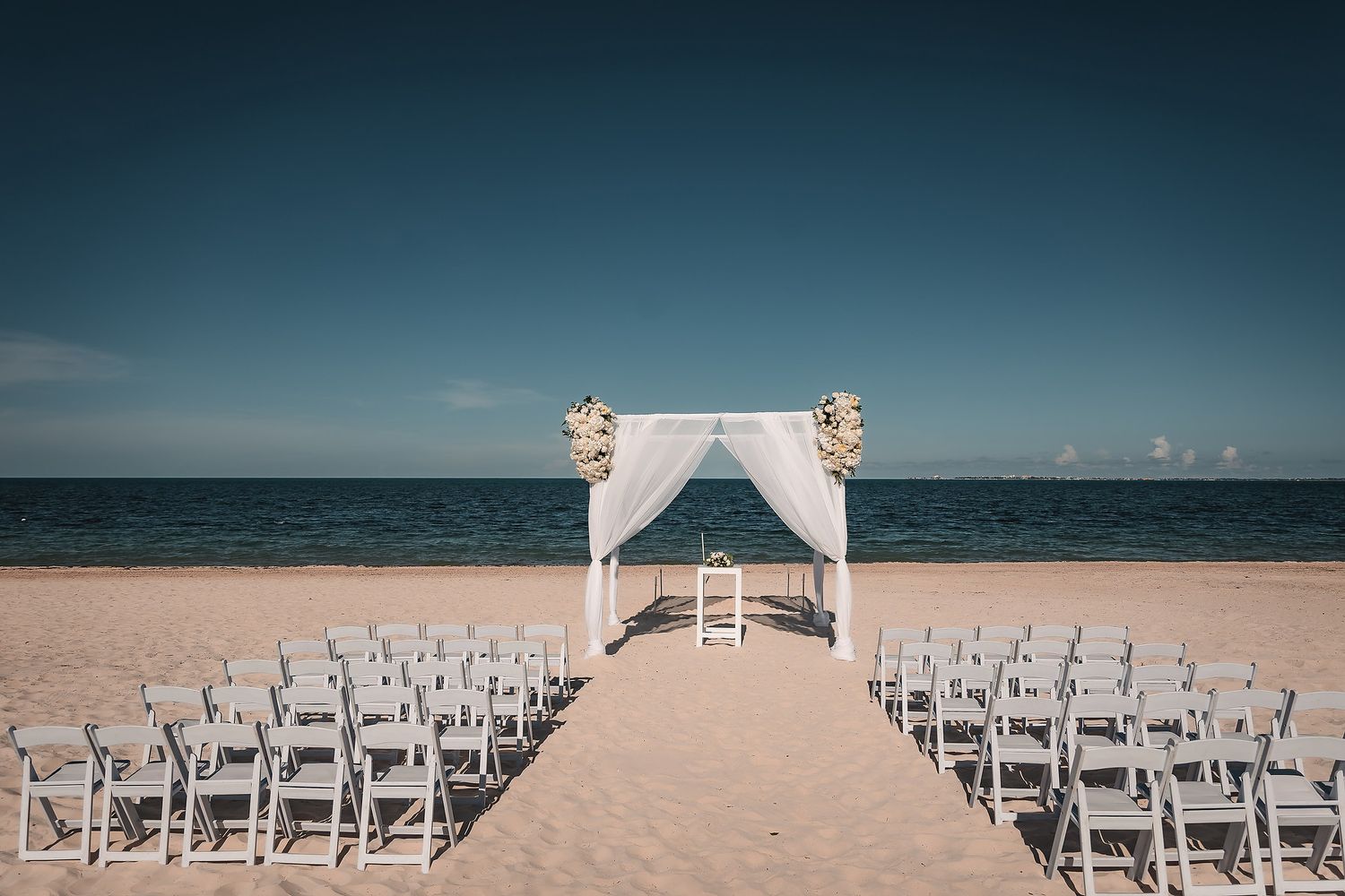 Beach wedding ceremony setup with white chairs and arch overlooking the ocean.