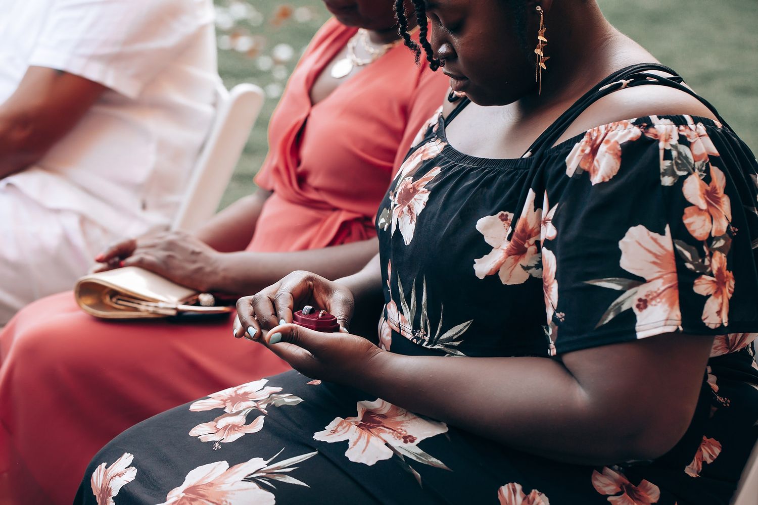 Person in floral dress using mobile phone while seated at outdoor gathering.
