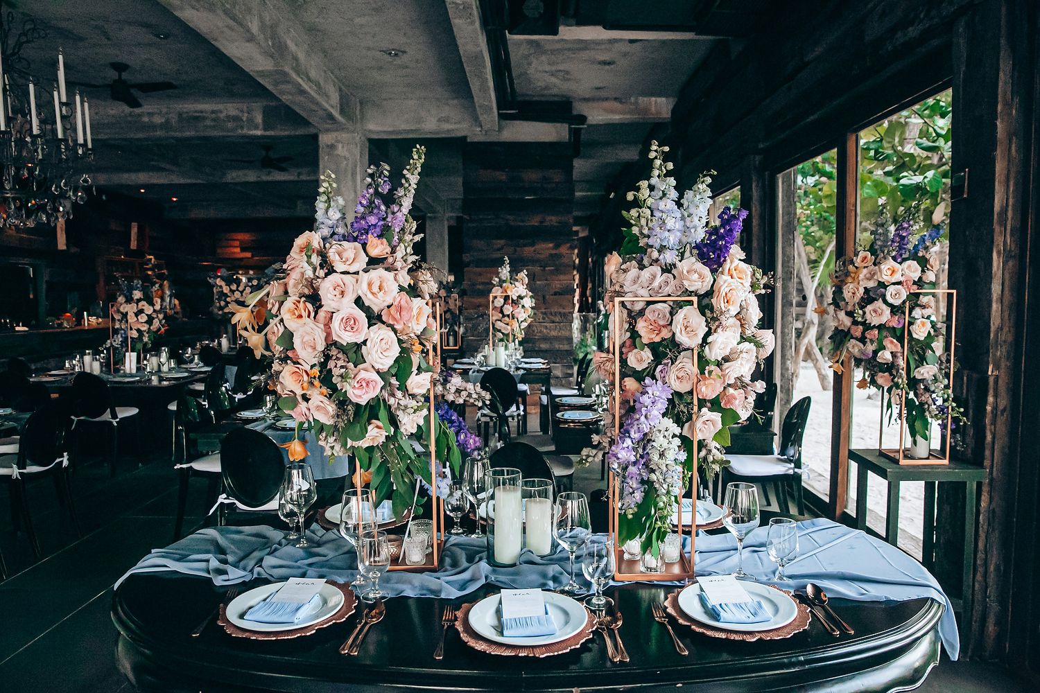 Elegant wedding reception tables decorated with floral centerpieces and candles in a rustic indoor venue.