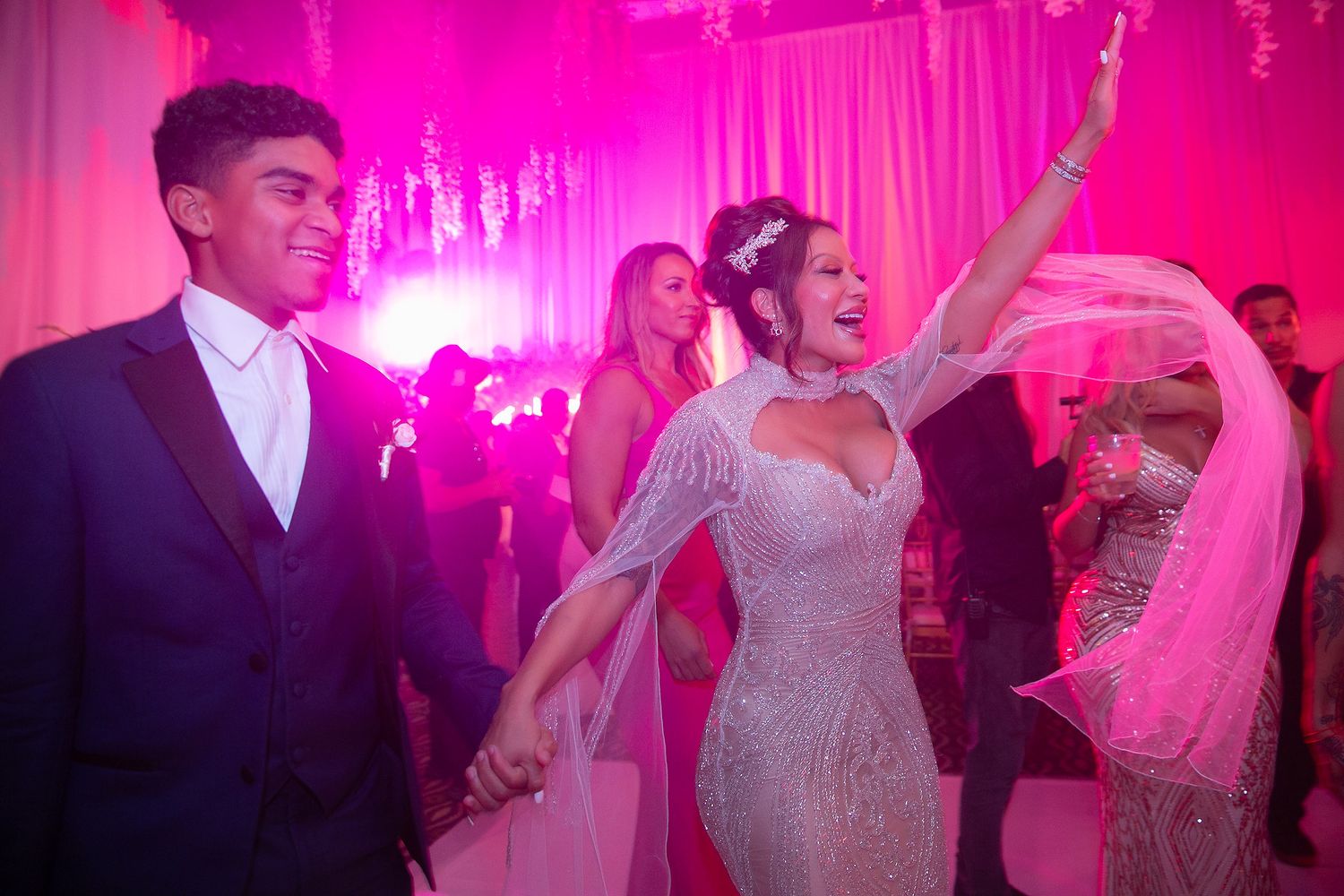 Wedding guests dance and celebrate on a pink-lit dance floor at an elegant reception party.