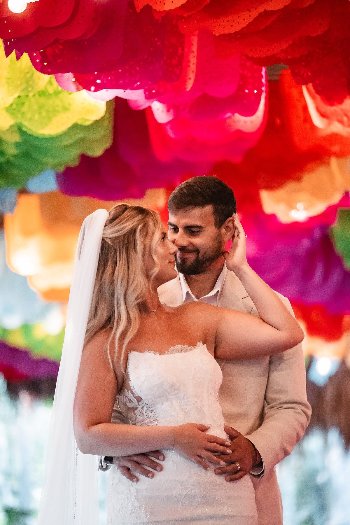 Newlyweds share an intimate moment under vibrant colorful decorations at their wedding.